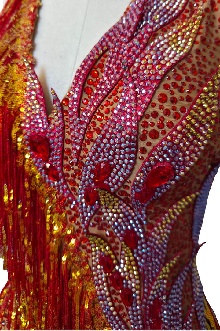 Macro close-up of Inferno Cascade Latin dress crystals and rhinestone embellishments in red and gold tones.