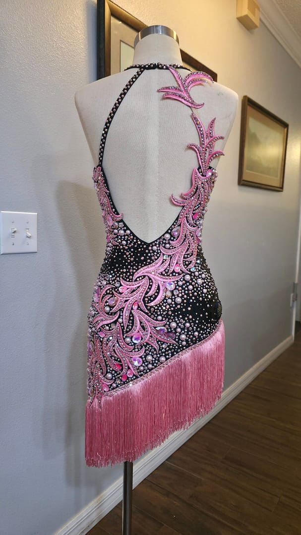 Back view of the Blush Noir Latin dress featuring an open-back design, pink crystal appliqué, and pearl embellishments.