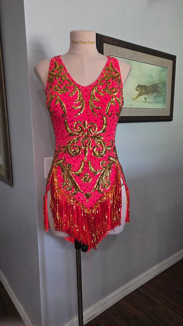 Professional dancer wearing the Gilded Heat – Performance Series Latin dance dress featuring vibrant neon pink fabric, gold embellishments, sparkling rhinestones, and dynamic fringe movement.
