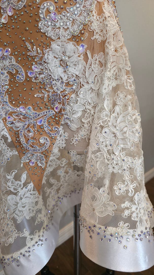 Close-up of the Lace Temptation dress skirt showing floral lace appliqué, crystal embellishments, and satin-trimmed hem