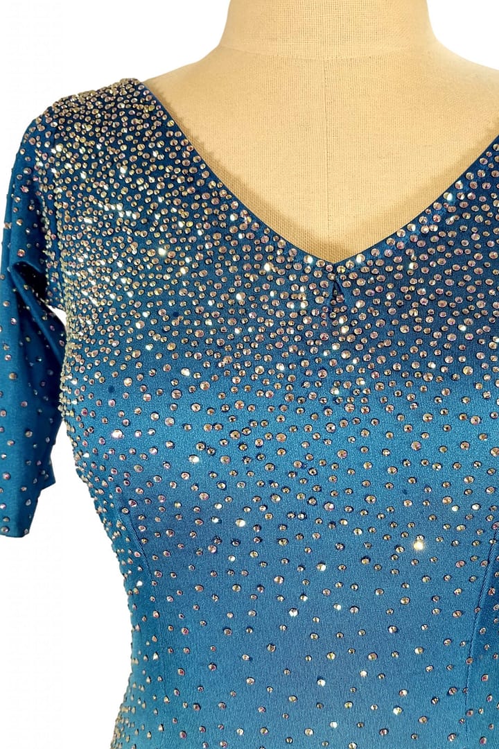 Blue fire ballroom gown — bodice detail — Close-up of the V-neckline showing heavy application of AB and blue rhinestones, densely covering the bright blue fabric and sleeves.