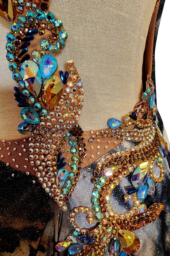 Kaya latin dress — stonework close-up — Extreme close-up of clustered gold and blue crystals in various shapes and sizes forming an ornate, swirling design.