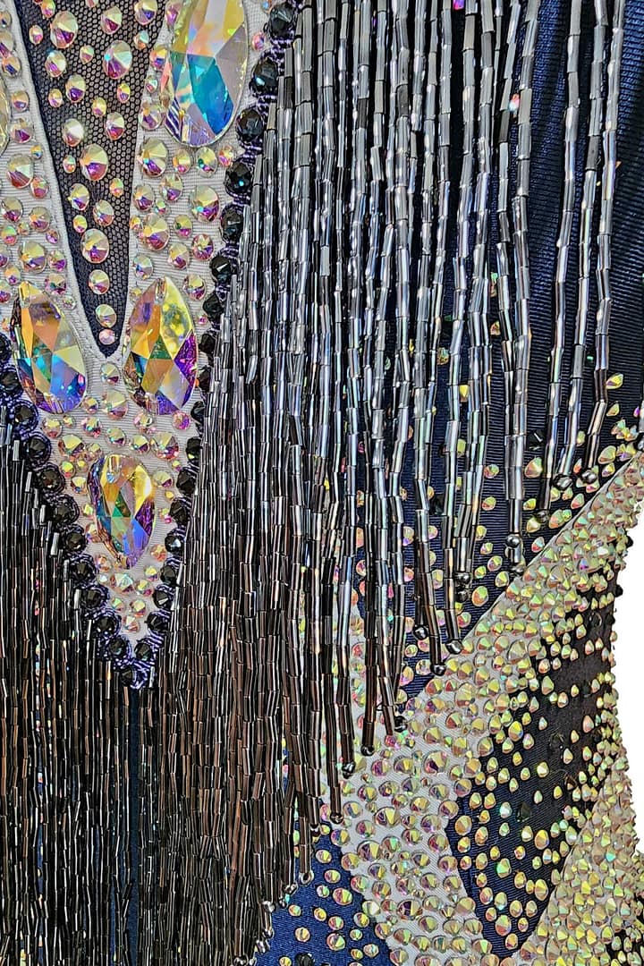 Arlan Latin dress — stonework close-up — detailed view of iridescent tear-drop crystals, black beads, and silver fringe against dark blue fabric.
