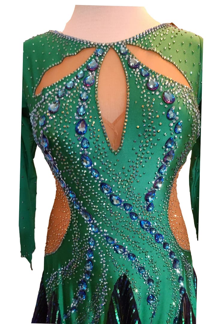Close-up of Emerald Majesty Signature Latin bodice with sapphire rhinestone swirl pattern, dense crystal placement, and emerald stretch fabric