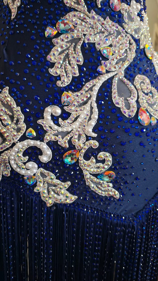 Close-up detail of Aurora Royale Latin dress showcasing iridescent crystals, pearl accents, sapphire rhinestones, and fringe trim.