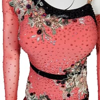 Bruna ballroom dress - detail view — close-up of coral-pink bodice with dense crystals, black sequin neckline, multicolored floral appliqués, and intricate beadwork on sheer mesh sleeve.