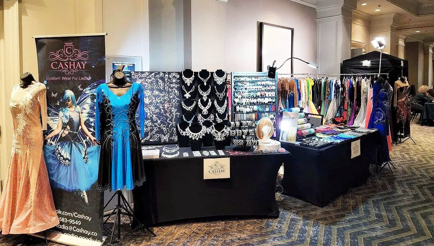 Cashay Design booth showcasing custom ballroom dance gowns, jewelry, and accessories for professional dancers.
