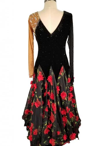 Fia ballroom gown — back view — The black and tan long-sleeved dress is shown from the back. It features a deep V-cut backline on the black velvet bodice. The skirt is black sheer fabric with red rose appliqués, continuing the theme from the front.