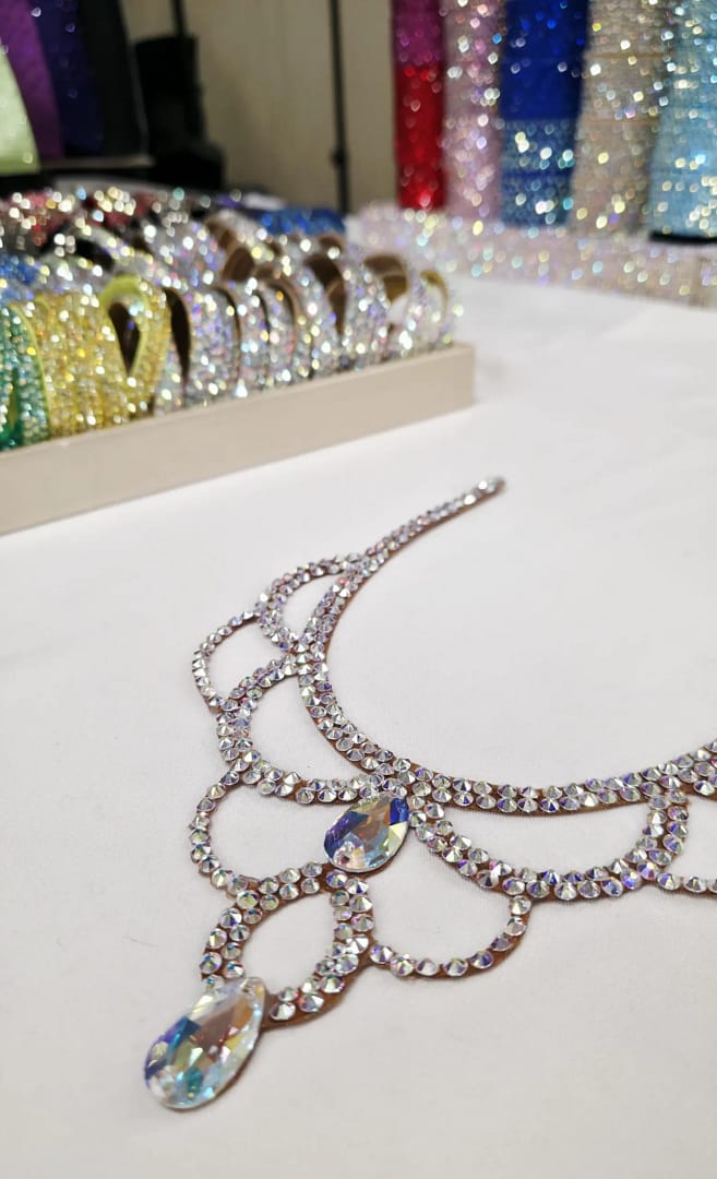 Angled flat lay of crystal ballroom necklace showing iridescent stones and scroll design