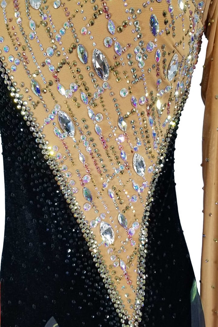 Fia ballroom gown — stonework close-up — Detail shot of the bodice showing the diagonal contrast between the heavily stoned tan mesh panel and the black velvet panel. The tan mesh is covered in lines of small rhinestones and large, clear iridescent teardrop and oval crystals.