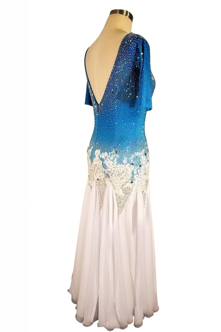 Blue fire ballroom gown — back view — Deep, low V-back bodice that mirrors the blue-to-white ombre and heavy crystal stoning, with white floral appliqué framing the waist.