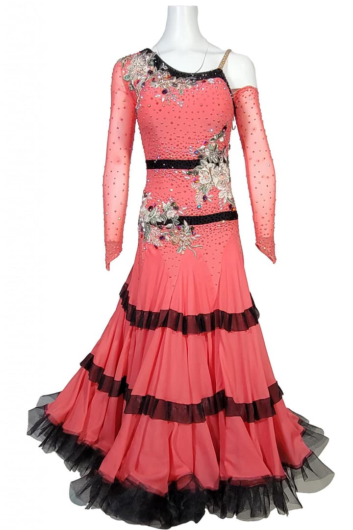 Bruna ballroom dress - front view – whole body — coral-pink ballroom gown with one-shoulder mesh sleeve, black sequin bands, crystal-covered bodice, floral appliqués, and layered black-trimmed ruffle skirt.