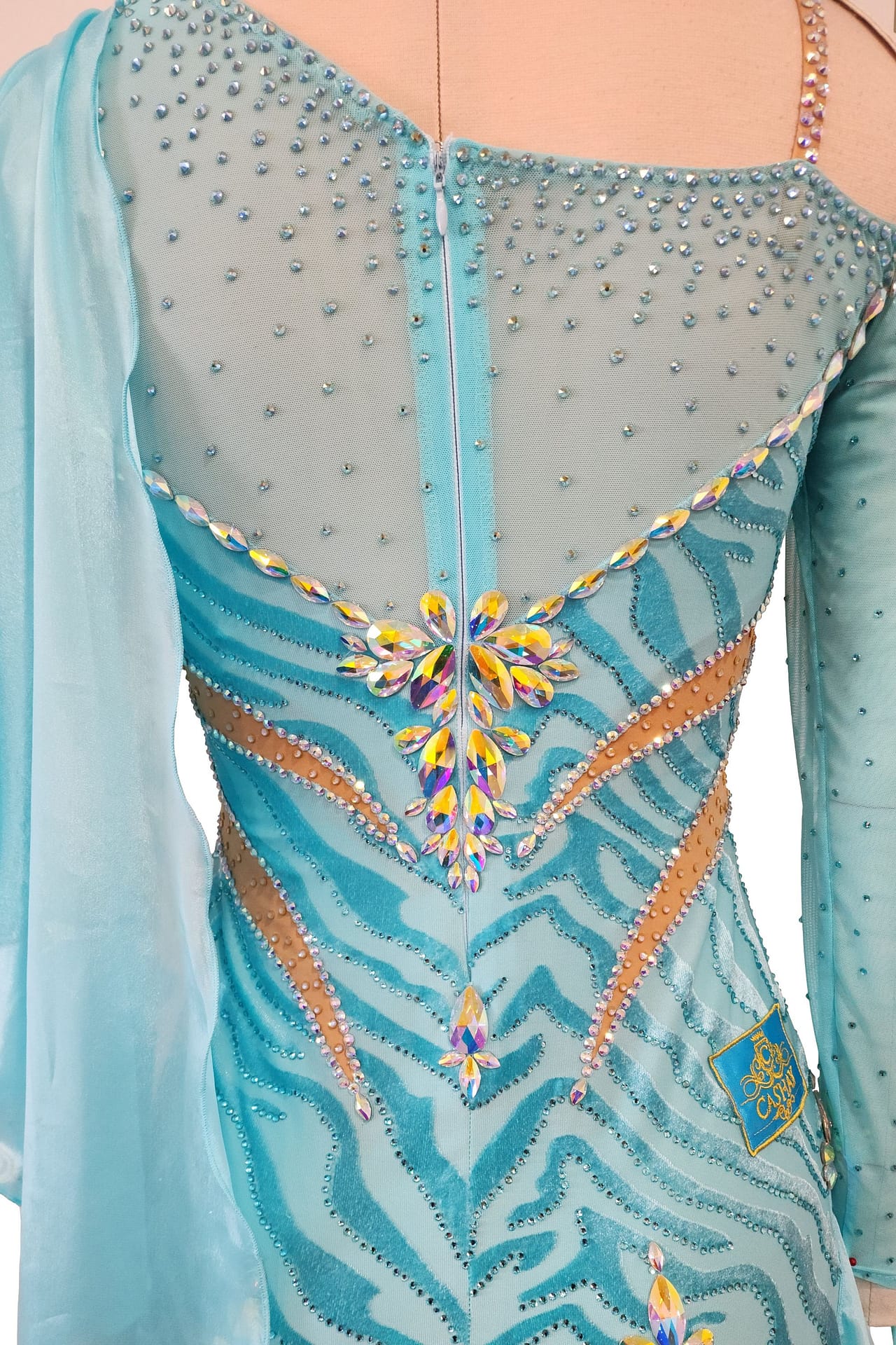 Azure Whispers Latin dress — close-up back view — Detailed shot of the blue zebra-print bodice, featuring large iridescent yellow and pink crystals centered above the zipper, accented by nude mesh cutouts.