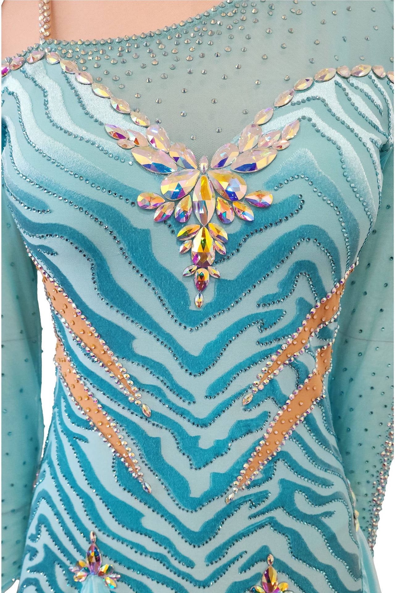 Azure Whispers Latin dress — bodice detail — close-up of light blue fabric featuring a zebra stripe pattern created by stoning, accented by peach trim and a large butterfly-shaped crystal cluster.