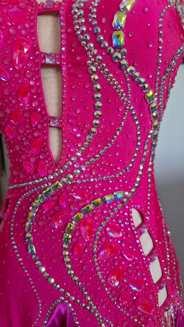 Close-up of Malibu Dream ballroom gown with hot pink fabric and dense rhinestone and crystal embellishments