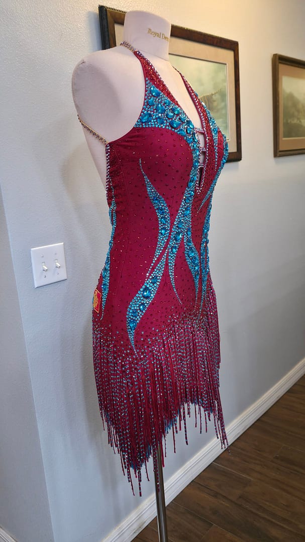 Front right view of the Crimson Mirage Signature Series Latin dance dress featuring aqua crystal detailing, plunging halter neckline, and asymmetrical fringe.