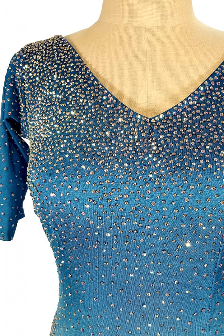 Blue fire ballroom gown — bodice detail — Close-up of the V-neckline showing heavy application of AB and blue rhinestones, densely covering the bright blue fabric and sleeves.