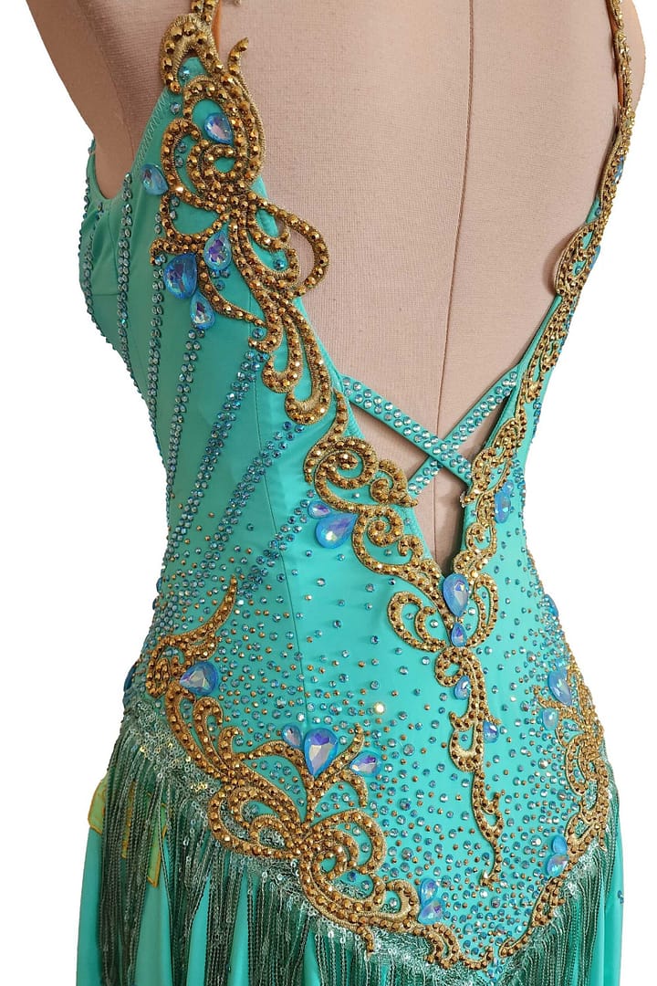 Ashcroft Latin Dress - Close-up side view of the teal Latin dress. Shows gold beaded scrollwork and criss-cross lower back detail.