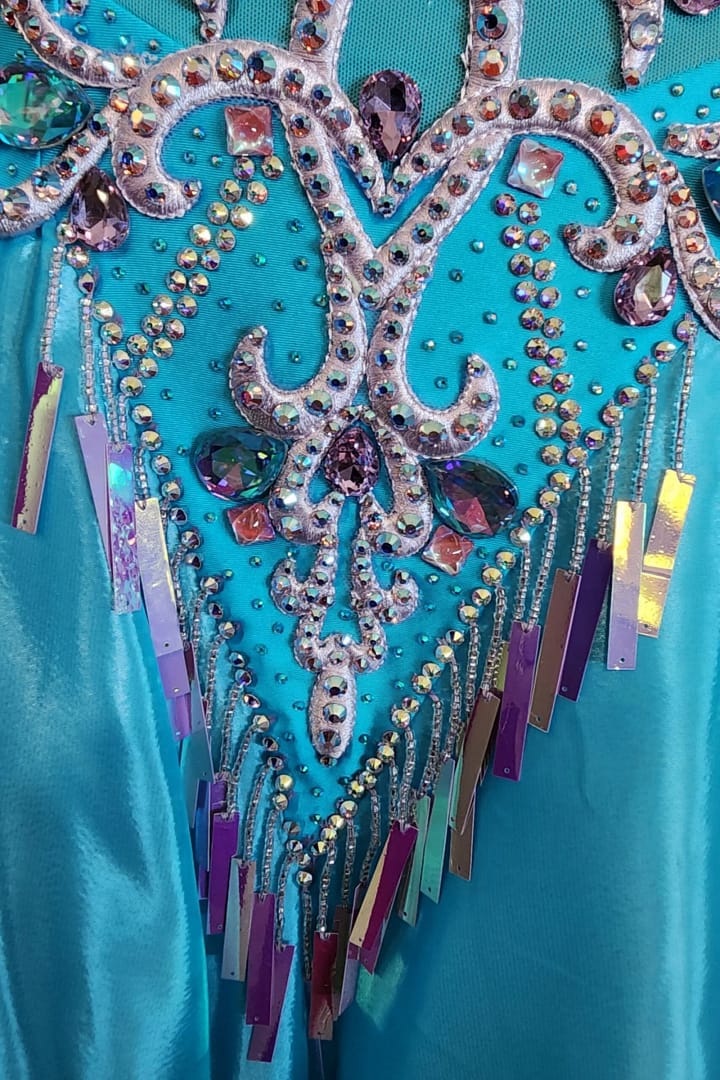 Jackie ballroom gown — stonework detail — close-up of the turquoise fabric, silver appliqué, iridescent teardrop gems, and hanging purple/silver holographic sequins.